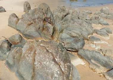 Büyük kayalar, kabuklar, mercan parçaları ve Tanjung Kalian Sahili yakınlarındaki dalgalar.