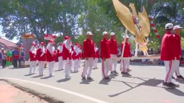MUNTOK, Indonezya - 15 Eylül 2023: Endonezya 'nın Bağımsızlık Günü' nde Kırmızı ve Beyaz Kostümlü Kartal Maskotunu taşıyan Bir Karnaval Katılımcıları Grubu