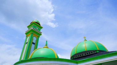 Bir caminin çatısı iki kubbe ve bir minareyle yeşildir.