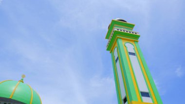 Parlak mavi gökyüzüne karşı yeşil bir kubbe ve bir caminin minaresi