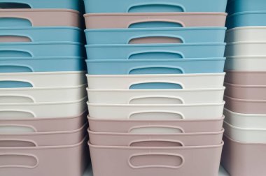 Kare şeklinde, çeşitli renklerde plastik sepetler, düzgün ve sıkıca bir rafa dizilmiş.