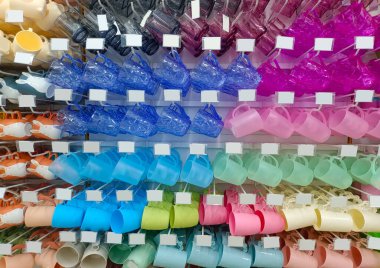 Parlak renkleri olan plastik bardaklar, cam bir dükkanın raflarında düzgün bir şekilde yerleştirilmiş.
