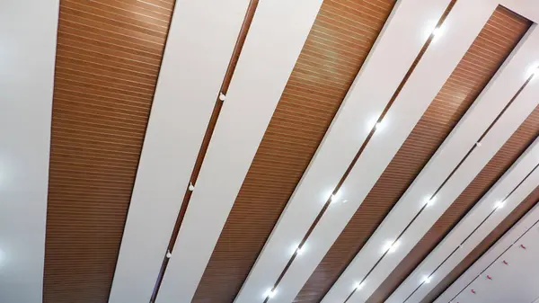 Işıkları ve beyaz ve kahverengi renklerin kombinasyonu olan çok amaçlı bir binanın içindeki tavan.