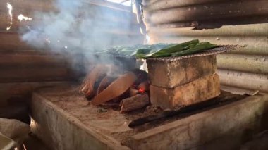 Muz yapraklarına sarılı işlenmiş işlenmiş bir Otak-otak yemeği, ahşap ateşli bir soba kullanılarak kızartılıyor.