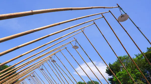 Çatı çerçevesinin altından, çaprazlanmış bambudan yapılmış birkaç asılı ışık ve mavi gökyüzü manzarası.