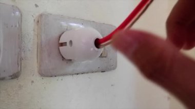 Bir adamın eli evdeki bir duvar prizinden bir elektrik prizinin fişini çekiyor.