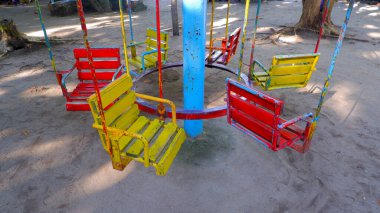 Tropik bir bahçede renkli ve unutulmaz bir atlıkarınca salıncağı. Salıncak ahşap ve metalden yapılmıştır. Kırmızı, sarı ve mavi renklerde boyanmıştır.