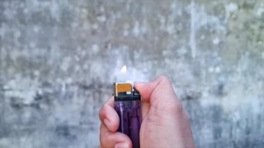 Bir adamın eski bir mor plastik çakmağı tutarken ve aydınlatırken çekilmiş 4K görüntüsü.
