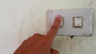 Işığı açmak için duvarın düğmesine dokunan bir adamın yakın görüntüsü.