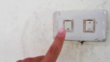 Işığı açmak için duvardaki düğmeye dokunan bir adamın yakın görüntüsü.