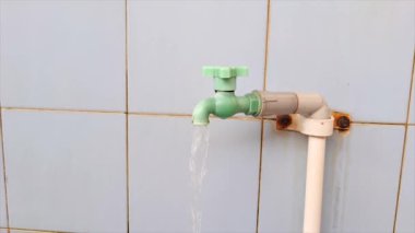 Yeşil kaplamalı bir duvarın karşısında akan yeşil musluğu kapatan bir adamın 4K görüntüsü.