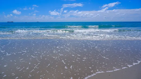 Açık mavi bir tuvalde bembeyaz bulutlarla süslenmiş kristal berrak suyla Tropikal Sahilin Doğal Manzarası
