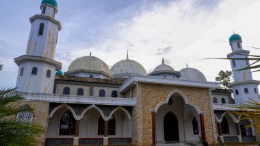 Cami 'nin ihtişamını kendine has mimari tarzıyla yakalayan alçak açılı bir çekim. Camide belirgin kubbeler ve parçalı bulutlu gökyüzüne karşı yükselen minareler yer alıyor..
