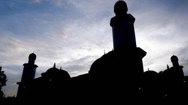 Bir cami kubbesinin silueti dramatik bir günbatımı gökyüzüne karşı. Bu görüntü, batan güneşin altın parıltısıyla, gün batımında İslam mimarisinin dingin güzelliğini yakalar..