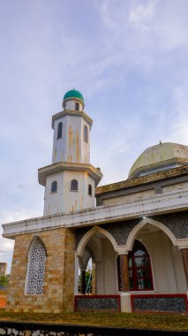 Cami 'nin ihtişamını bir minareyle ve merkezinde küçük bulutlu bir gökyüzüne karşı kendine özgü yeşil kubbesiyle yakalayan alçak açılı bir çekim..