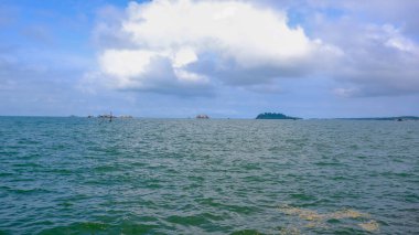 Geniş gökyüzünün altında sakin ve geniş bir deniz manzarası uzanır, tüylü bulutların tembelce sürüklendiği, aşağıdaki sakin sulara gölgeler düşürdüğü yerde..