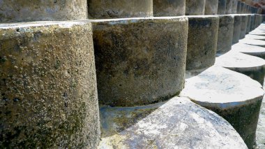 Yıpranmış beton deniz bariyerinin yakın plan çekimi silindirik çizgiler halinde tekrarlanarak derinlik ve doku hissi yaratıyor..