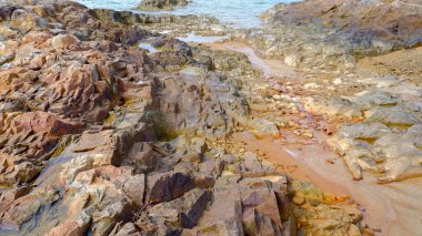 Açık bir günde kayalık kıyı şeridinin havadan görüntüsü. Saf kayalıklar, desenli yüzeyler ve kıyı boyunca değişen kahverengi ve gri tonlarıyla