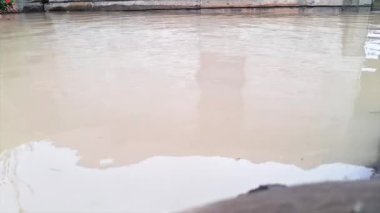 Yüzeyinde evleri yansıtan bulanık beyaz bir renkle dalgalanan bir sel havuzu.