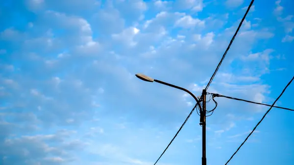 Açık ve bulutlu bir arka planı olan sokak ışıkları. Lamba merkezde, bir ampul içeriyor ve çeşitli yönlere uzanan birkaç kabloya bağlı..