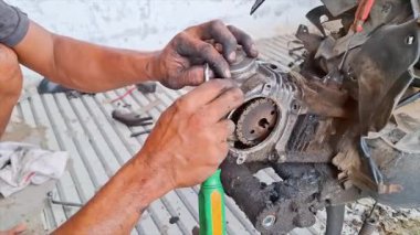 Motosiklet motorunu tamir eden bir tamircinin ellerine yakın çekim. Elleri yağ içinde, bu da sürecin ne kadar sıkı çalıştığını gösteriyor. Motor parçaları görünür. Karmaşık detayları gösteriyor.