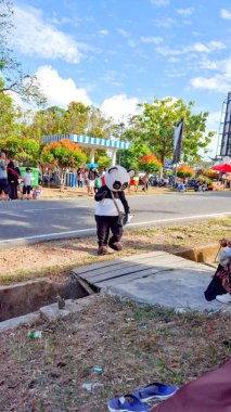 MUNTOK, INDONEZYA - 21 YIL 2024: Açık bir mahallede panda kostümü giyen bir kişi yolun kenarında duruyor