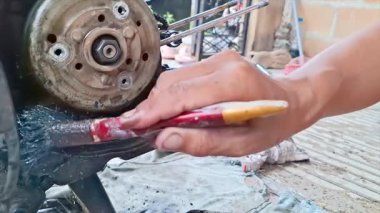 Motosiklet motorunun karmaşık kısımlarına küçük bir fırçayla yağ sürerken bir tamircinin eline yakın çekim. Metalden yapılmış motor parçaları ve aşınma izleri. 