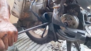 Bir tamircinin eli uzun bir T-anahtarı kullanarak motorun motor bloğunun kenarındaki sürgüyü açmaya çalışıyor.