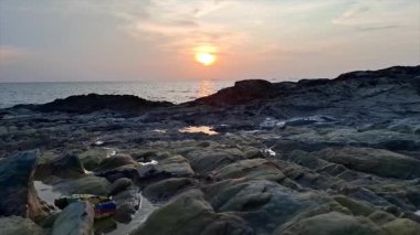Gün batımında sakin ve güzel bir deniz manzarası. Ön planda sert ve karanlık kayalar ve gelgit havuzları var..