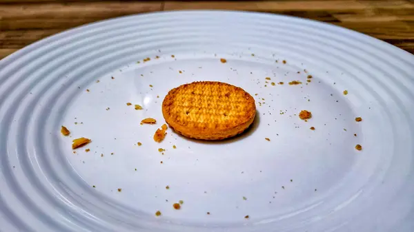 Dağınık kırıntılarla çevrili beyaz bir seramik tabağın ortasına yerleştirilmiş tek bir altın pastanın yakın çekimi..