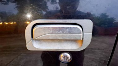 Entegre kilit silindirli gümüş metalik bir araç kapı kolunun koyu yansıtıcı bir yüzeye monte edilmiş detaylı yakın plan görüntüsü.