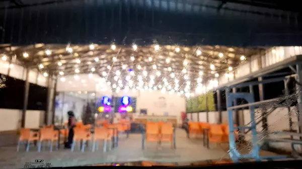 Turuncu sandalyeli, dekoratif ışıkları olan, geceleri hafif ıslak bir arabanın ön camından görünen rahat bir kafeterya..