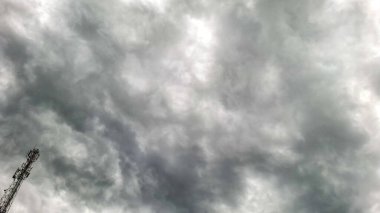 Koyu gri fırtına bulutları gökyüzünü kaplıyor ve köşede bir iletişim kulesi görünüyor. Kalın bulut oluşumu dramatik ve yoğun bir atmosfer yaratır..