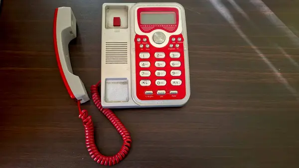 Koyu ahşap bir yüzeye yerleştirilmiş klasik kırmızı ve gümüş kablolu telefonun üst görüntüsü