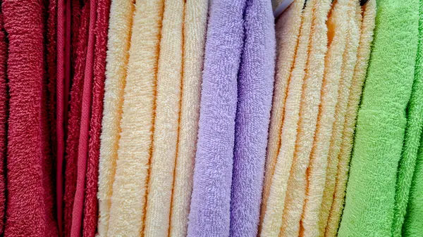 Turuncu, yeşil, mavi ve kırmızı da dahil olmak üzere çeşitli yumuşak ve ılık renklerde düzgünce katlanmış ve istiflenmiş havlular. Havlunun yumuşak dokusu açıkça görülüyor, rahat bir ortam yaratıyor ve... 