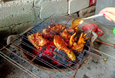 Geleneksel ızgara baharatlı tavuk parçaları ve kırsal bir metal ızgarada kızgın kömürde pişirilen tavuk ayaklarının yakın plan görüntüsü.