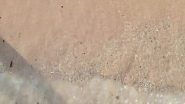 Küçük, yumuşak bir okyanusun kumlu bir sahile doğru yavaşça dalgalanmasının yakın çekim görüntüleri..
