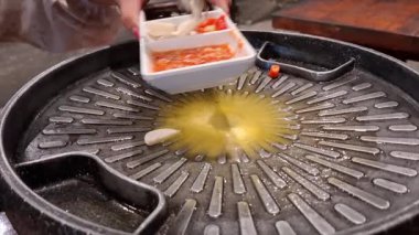 Görüntüler Kore barbekü pişirme sürecinin başlangıcını gösteriyor. Sarımsak dilimleri ve baharatlı biber sosu eritilmiş tereyağlı ızgara tavaya dökülüyor..