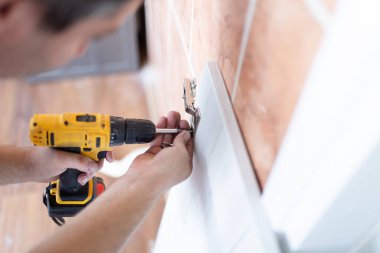 Man Assembling Shelf Using Electric Drill Tool At Home. Male Housework And House Furnishing. Handyman Fixing Wooden Cabinet During Renovation