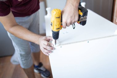 Man installing new furniture at his home and using cordless screwdriver