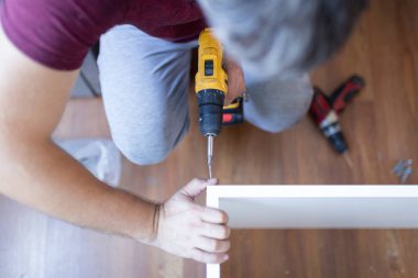 Man installing wooden shelves by using cordless screwdriver