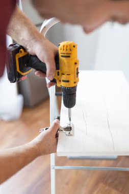 Close up of man assembling furniture by using cordless screwdriver