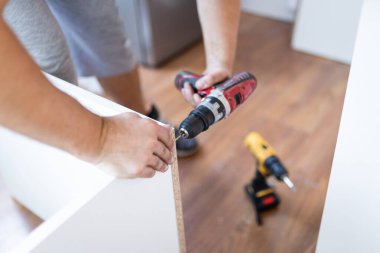 Handyman at work. Repairing kitchen shelves with cordless screwdriver