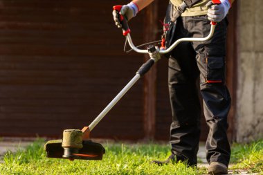 Worker with electric mower in his hands, mowing grass in front of the house.