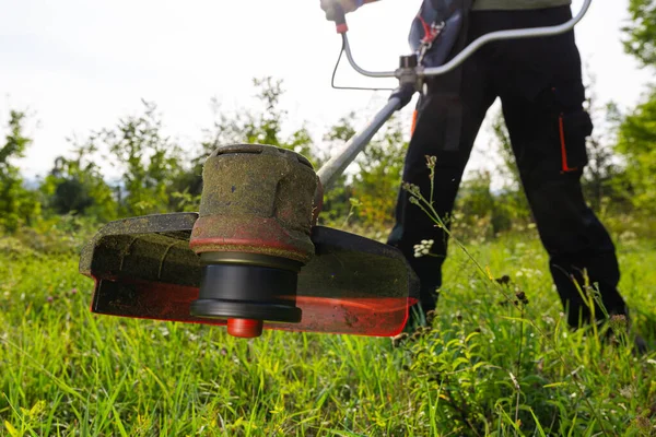Close up of string grass cutting trimmer held by worker in protective clothing. Gardening concept.
