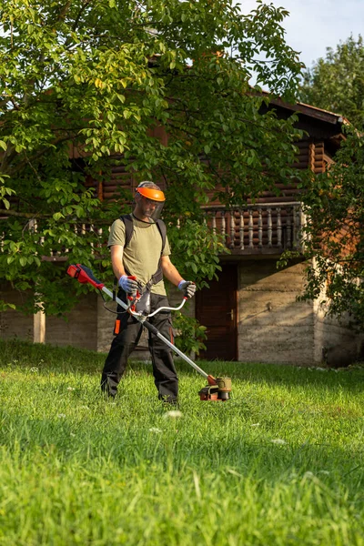 Landscape maintenance concept. Man cutting grass in yard by using electric string grass trimmer.