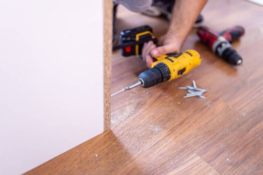 Close up of handyman using electrical screwdriver to install wooden shelf.