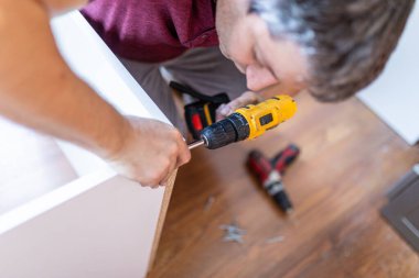 Handyman at work. Repairing kitchen shelves with cordless screwdriver