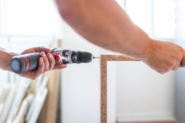Close up of worker installing kitchen shelf by using cordless screwdriver at home. Space for copy.