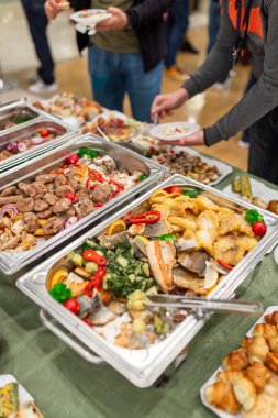 Warming dishes with food and people serving themselves. Buffet event concept.